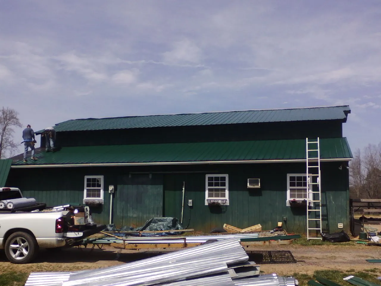 Crew installing green metal roofing on a large green barn in Sheridan